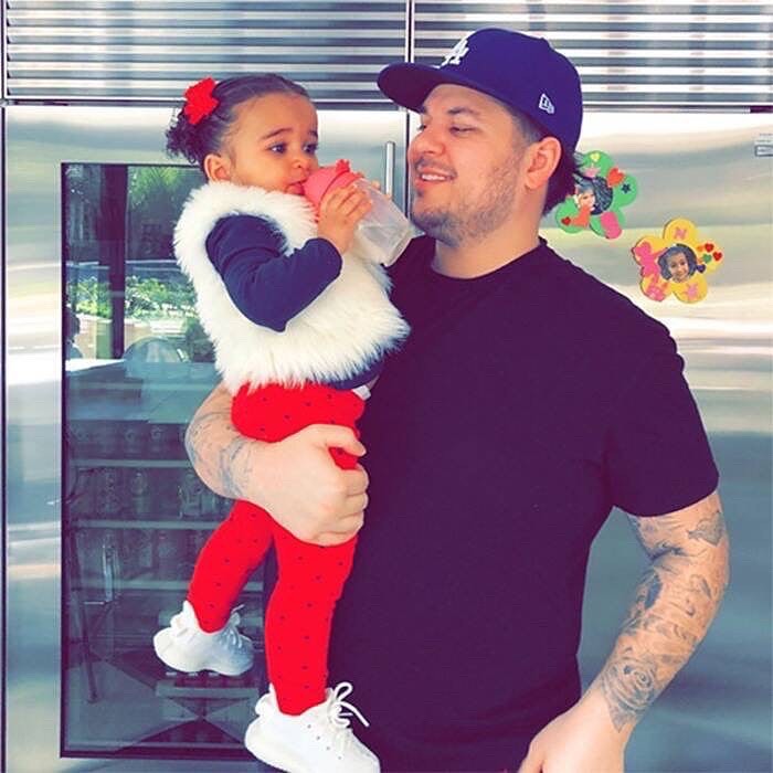 Rob Kardashian holds his daughter, Dream Kardashian, who is drinking from a bottle.