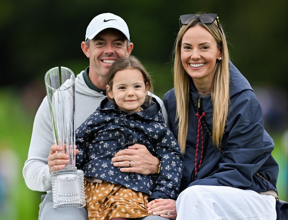 Rory McIlroy celebrates his win with his wife Erica and daughter Poppy, holding the Amgen Irish Open Championship trophy.