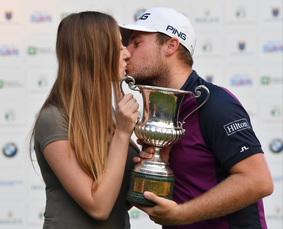 Tyrrell Hatton kisses girlfriend Emily Braisher while holding The Italian Open trophy.