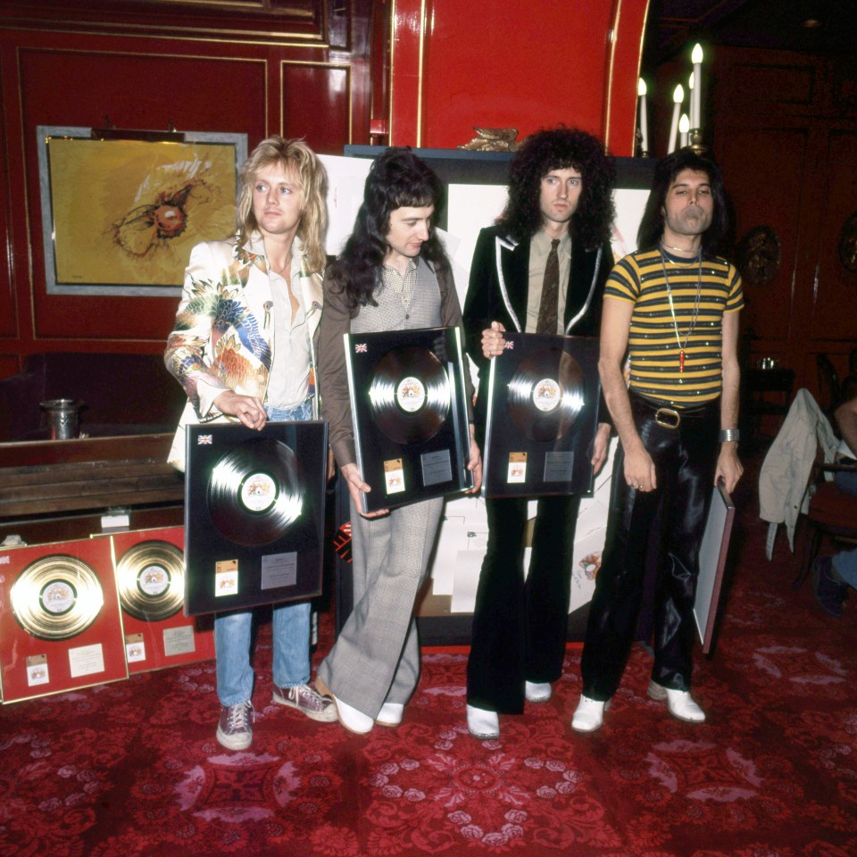 Members of Queen holding Silver, Gold, and Platinum records.