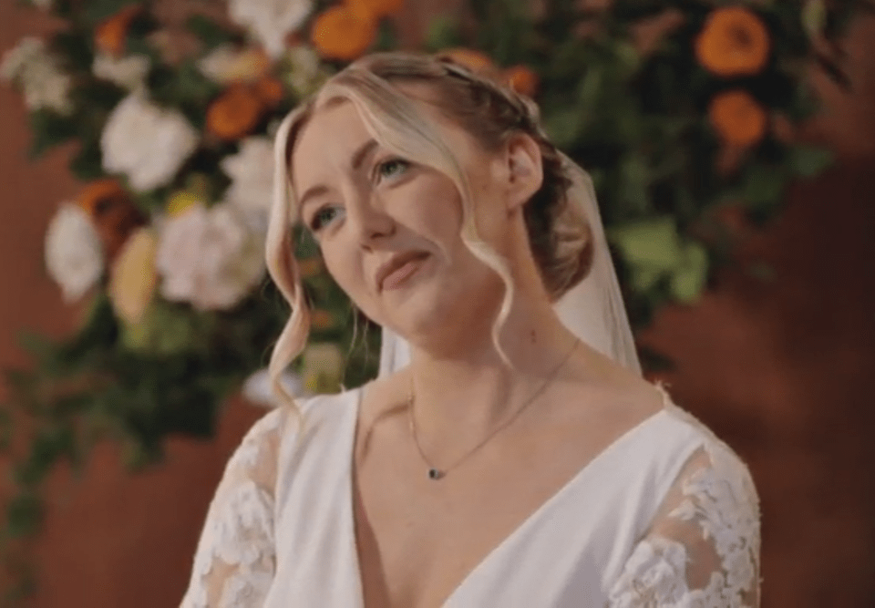 A bride in a white dress with lace sleeves and a delicate necklace looks away from the camera.