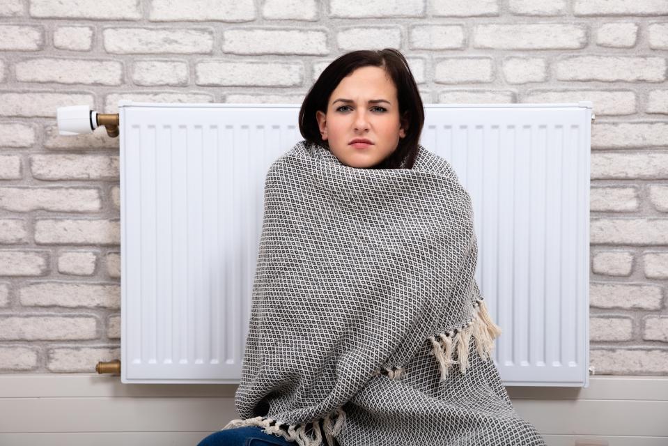 RJW8AC Young Woman Wrapped In Blanket Sitting Near Radiator At Home