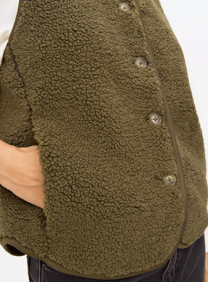 Person wearing a dark olive green fleece vest with a hand in the pocket.