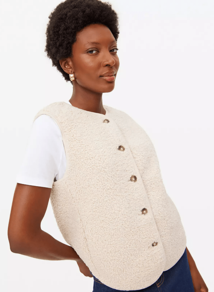 A woman wearing a cream-colored sherpa vest over a white t-shirt.