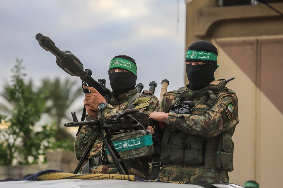 Two members of the Al-Qassam Brigades, Hamas's military wing, in camouflage and balaclavas, one holding a rocket-propelled grenade and the other a machine gun.