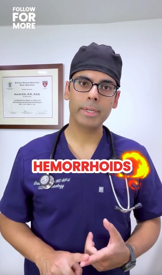 Video still of Dr. Saurabh Sethi, a gastroenterologist, wearing a blue scrub and black surgical cap, with the text "HEMORRHOIDS" in red and orange flames overlaying his chest.