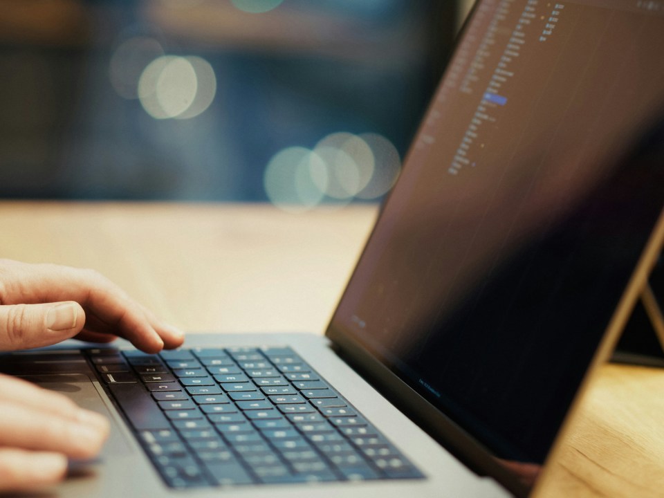 Person typing on a laptop with code on the screen.