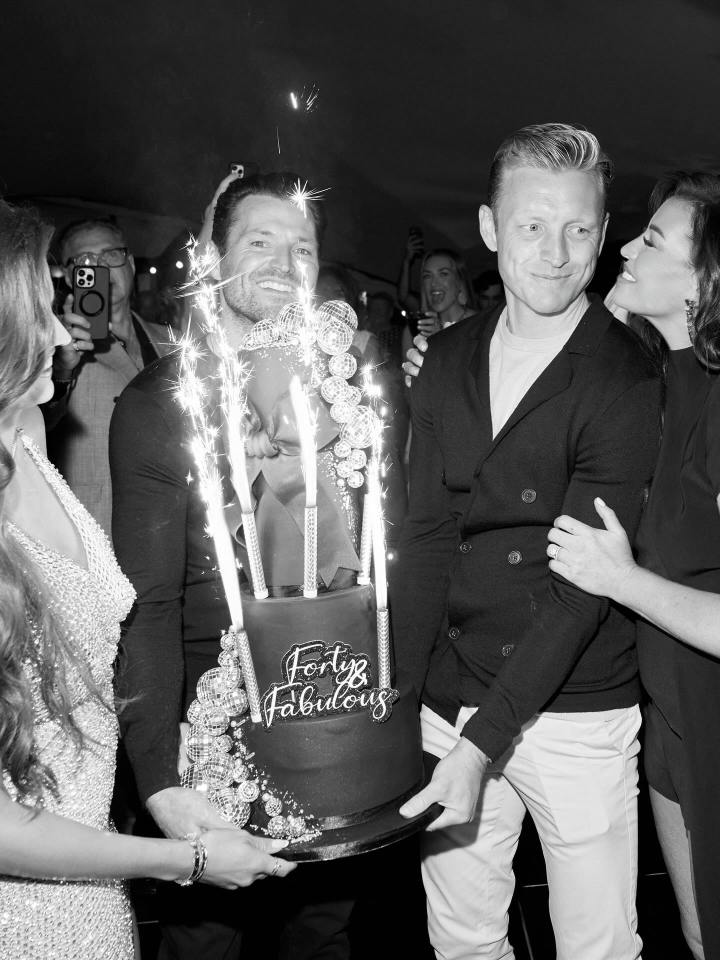 Black and white photo of a man smiling as he holds a "Forty & Fabulous" birthday cake with sparklers.