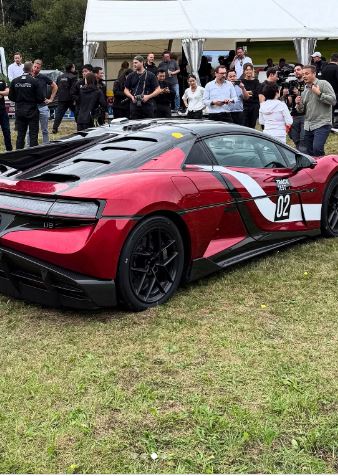 Red Yangwang U9 Xtreme supercar on a grassy field with people in the background.