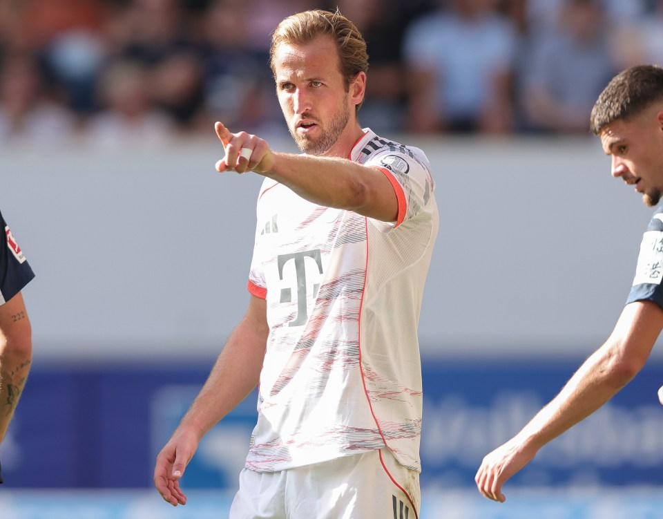 Harry Kane in a white FC Bayern München jersey, pointing with his right hand.