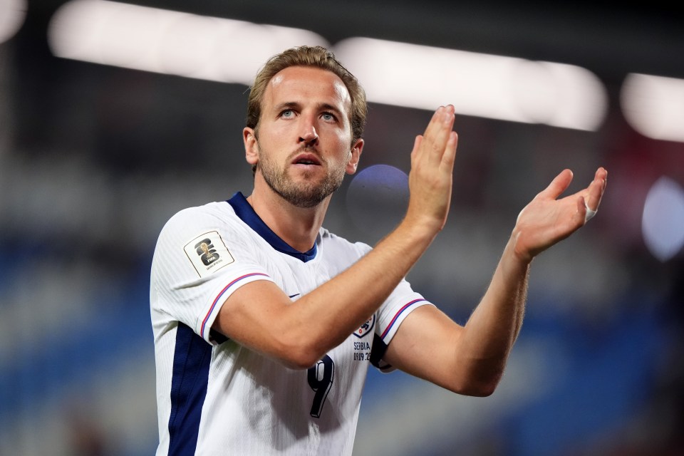 Harry Kane, wearing a white jersey with a FIFA Qualifiers patch, looks up and claps with both hands.