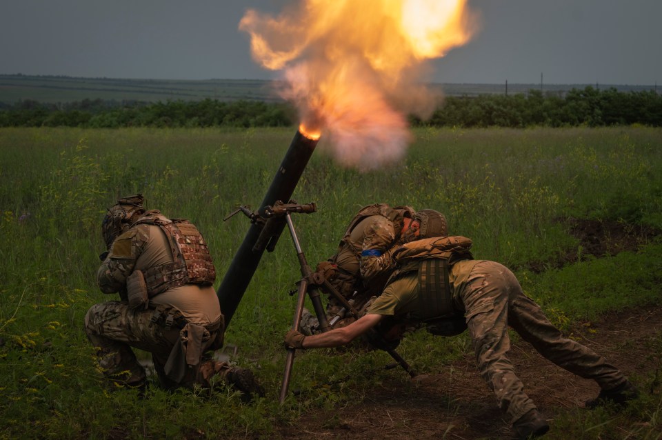 Two Ukrainian soldiers firing a mortar with a bright flash of light and smoke.