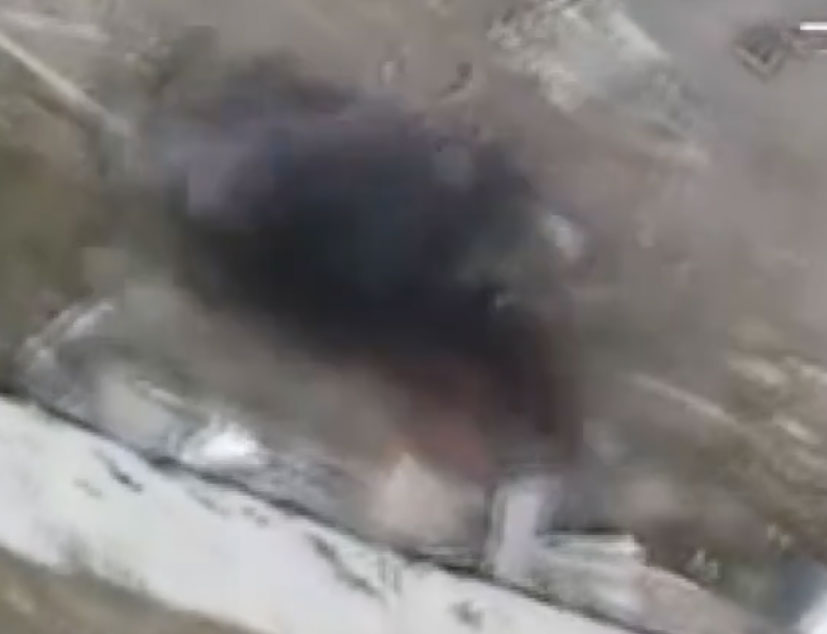 Footage of a military tank under fire with smoke and debris around it.
