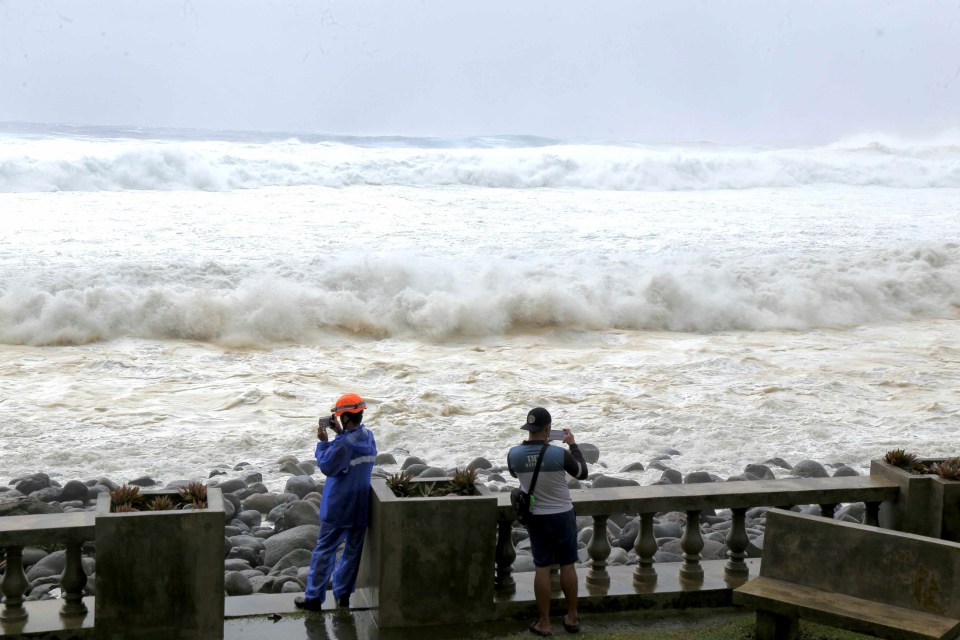 Two people capturing a video of strong waves battering the coast.