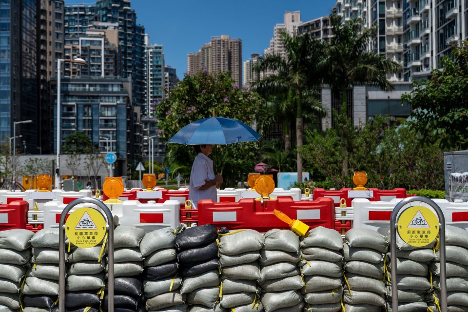 A person holding a blue umbrella walks past barricades and sandbags in Tseung Kwan O District in preparation for Typhoon Ragasa.