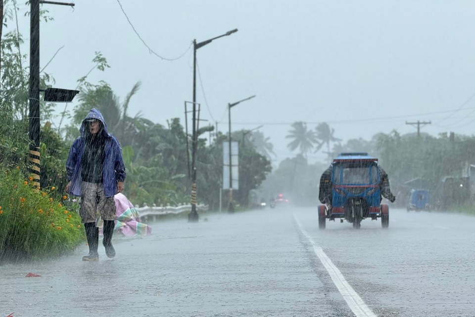 A person in a blue rain jacket walks along a road during heavy rain from Super Typhoon Ragasa in Lal-lo town, Cagayan province.