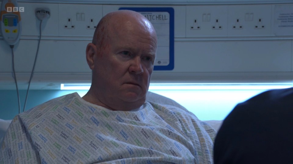 Phil Mitchell from Eastenders, in a hospital gown, looking serious with scratches on his head.