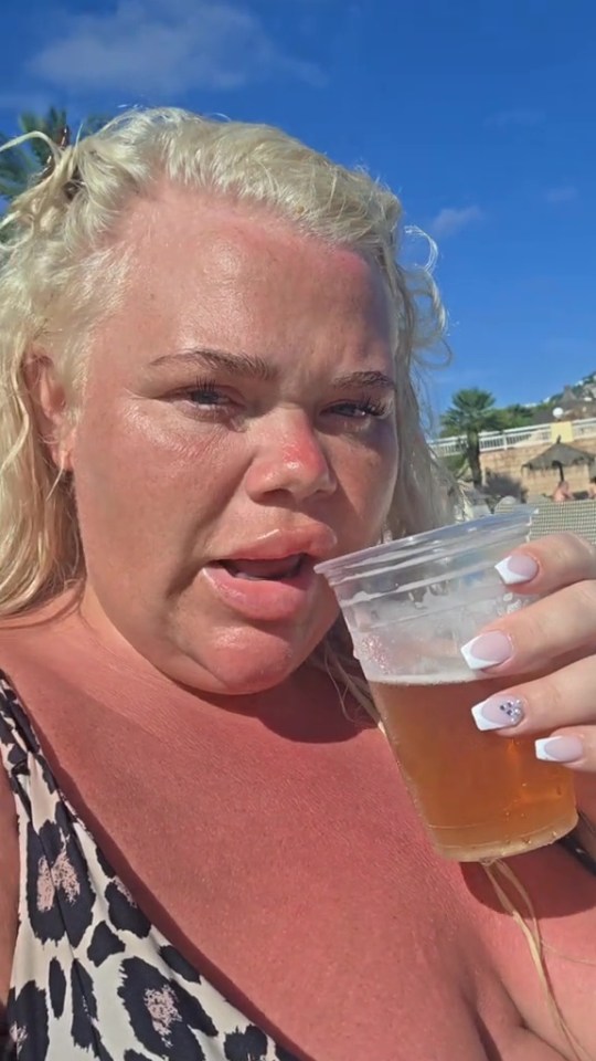 A woman with sunburned skin and blonde hair holding a drink.