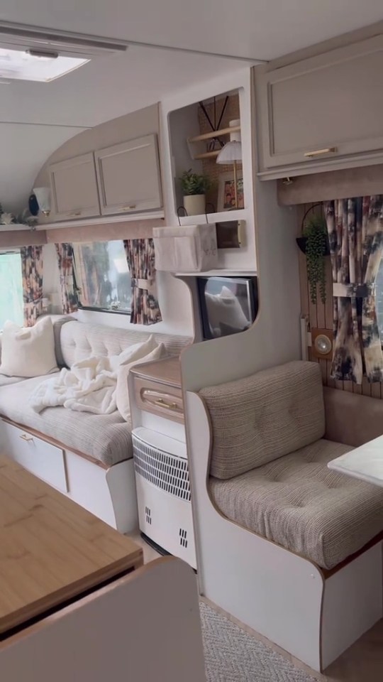 A renovated caravan interior with light-colored furnishings, patterned curtains, and a small television.