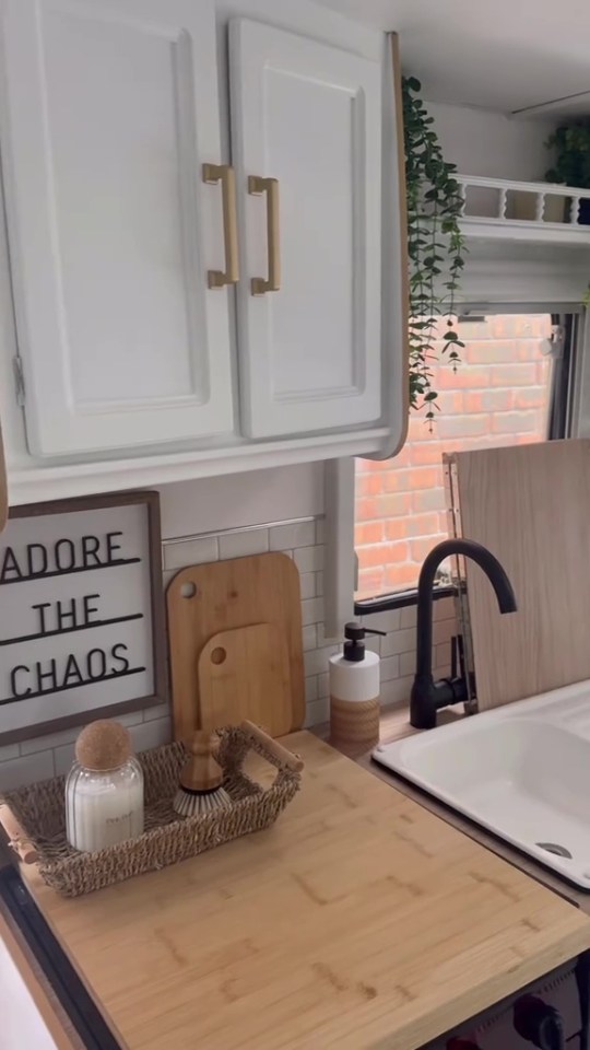 Kitchenette with white cabinets, light wood counters, a black faucet, and a small sign that reads "ADORE THE CHAOS."