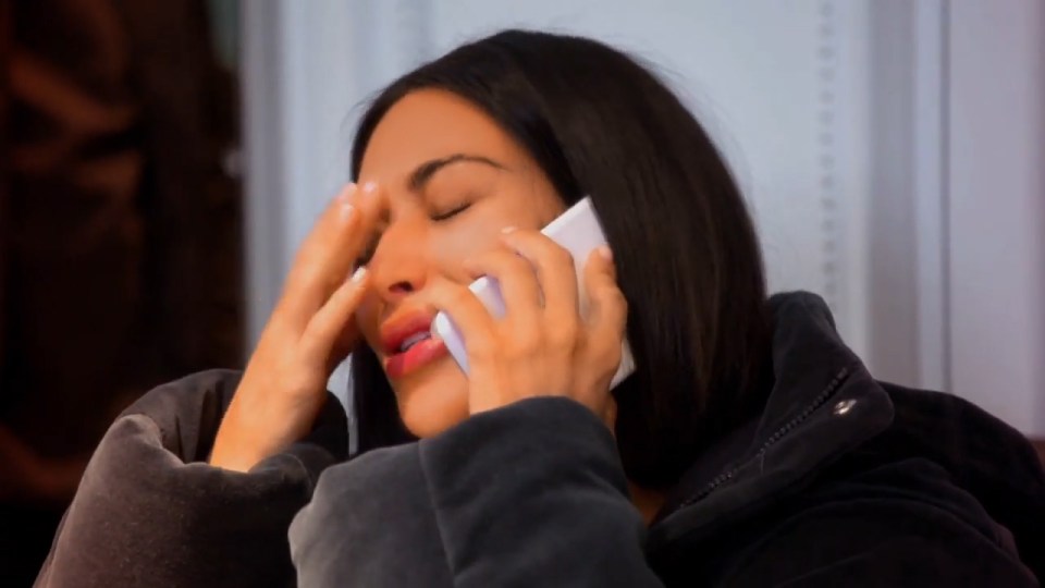 Kim Kardashian crying while on the phone, covering her face with her hand.