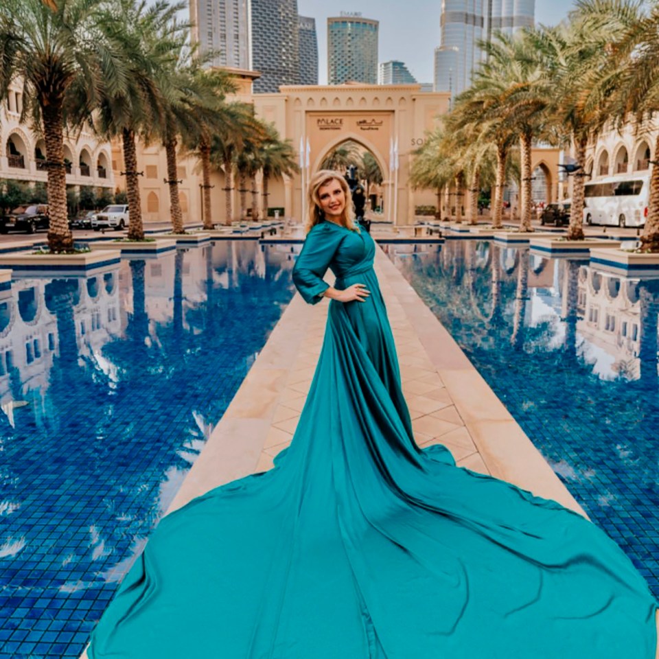 Anastasiia Chikina, 32, a Russian mother, standing next to a large pool with palm trees, buildings, and an ornate archway in the background.