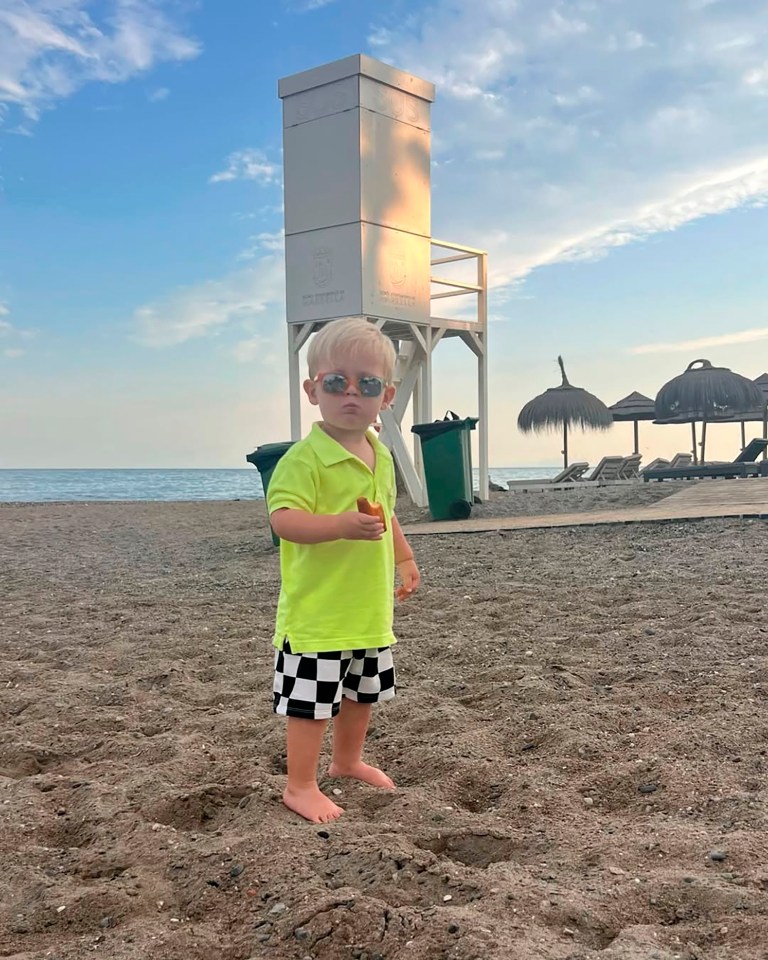 Oliver Pugh, a young boy with blonde hair and sunglasses, standing on a beach in Marbella, Spain.