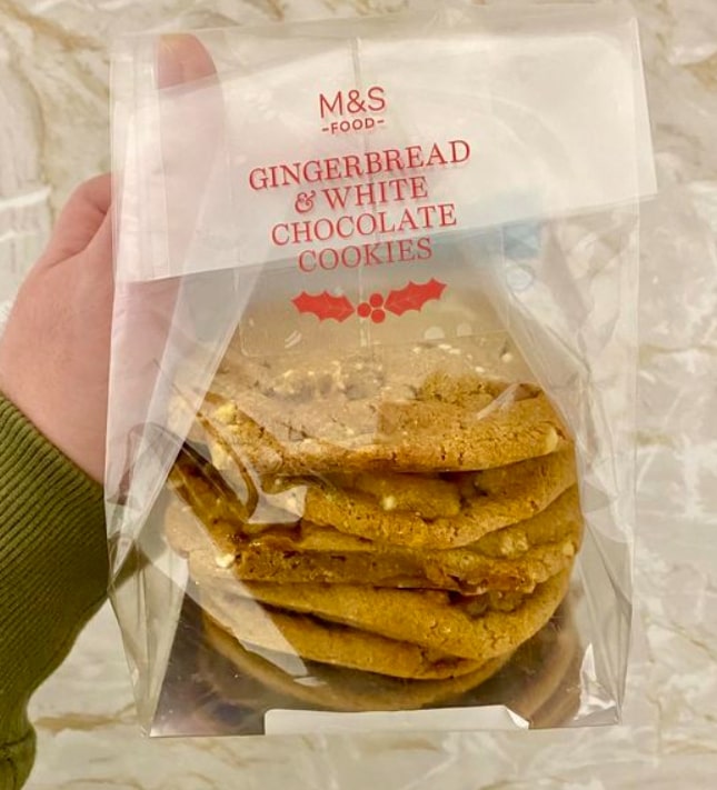 A clear plastic bag of M&S Food Gingerbread & White Chocolate Cookies with a holly illustration.