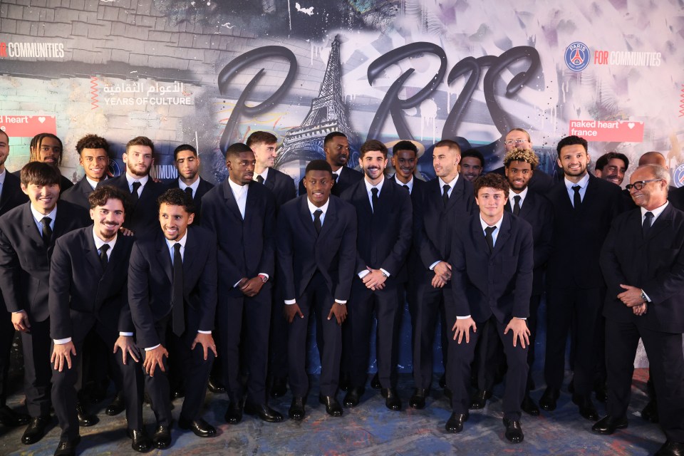 A group of men in dark suits and black ties pose for a photo in front of a graffiti-style mural of "Paris" and the Eiffel Tower.