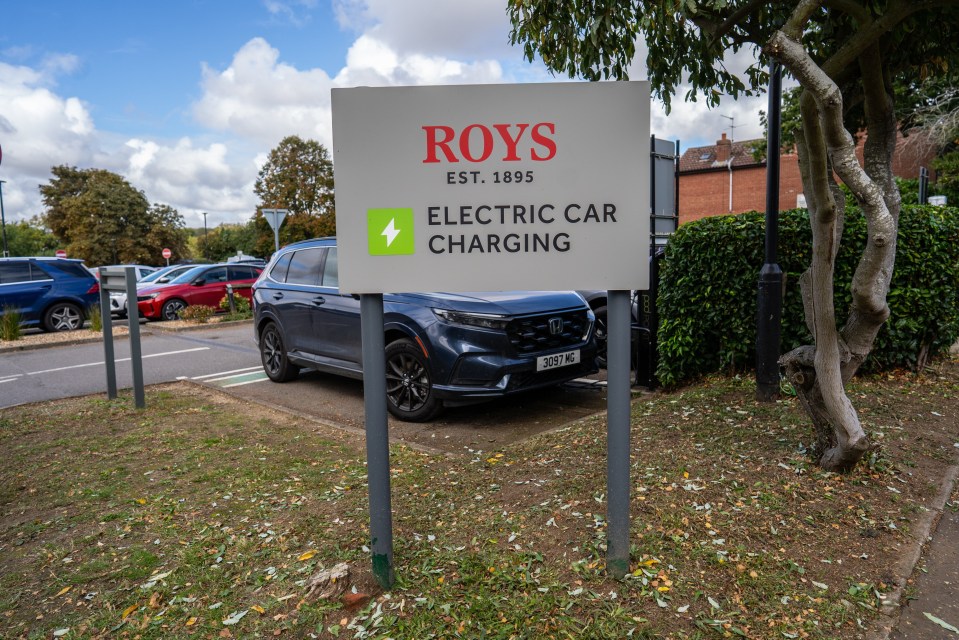 Roy's Electric Car Charging sign with a dark blue SUV charging in the background.