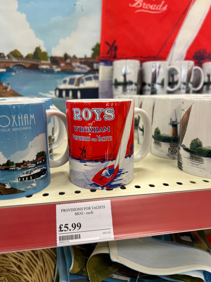 Mugs with images of the Norfolk Broads, including one red mug labeled "Roys of Wroxham Provisions for Yachts" and priced at £5.99.