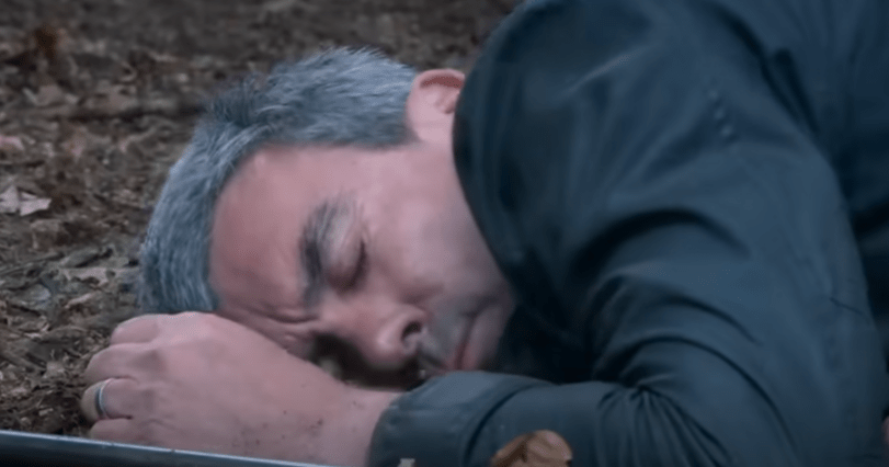 Man with graying hair lying on the ground, seemingly unconscious or dead.