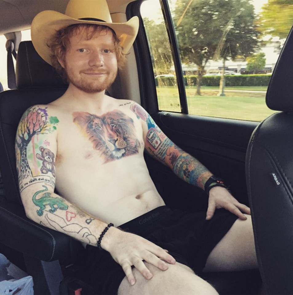 Ed Sheeran showing off his new lion tattoo on his chest, sitting in a car wearing a cowboy hat.