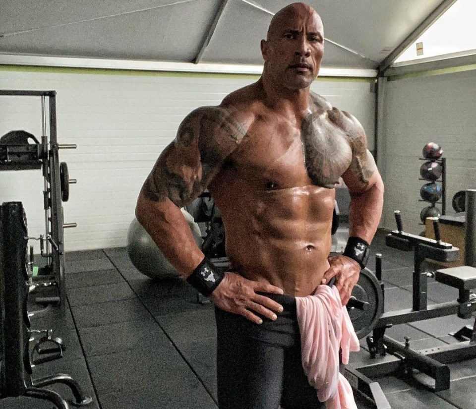 Dwayne "The Rock" Johnson posing shirtless in a gym.