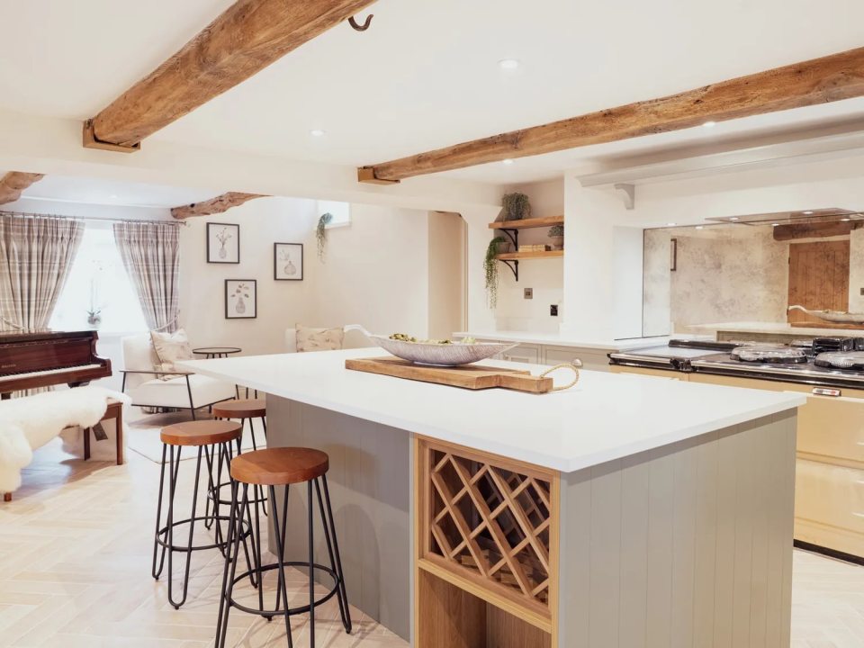 Open-plan kitchen and living area with exposed wooden beams, an island with bar stools, and a piano.