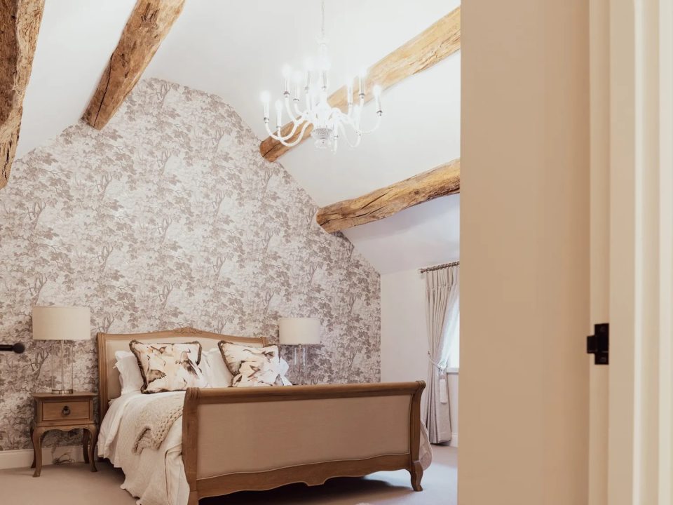 Bedroom at Stag Cottage with a double bed, patterned wallpaper, and exposed wooden beams.