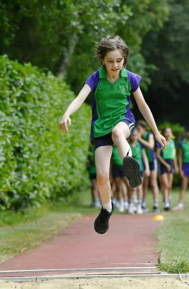 Sienna performing a long jump in her school uniform.