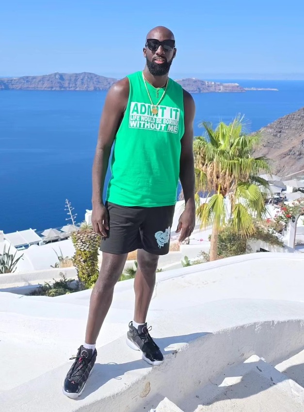 Orson Nurse posing in a green tank top with text "ADMIT IT LIFE WOULD BE BORING WITHOUT ME" overlooking the Aegean Sea.