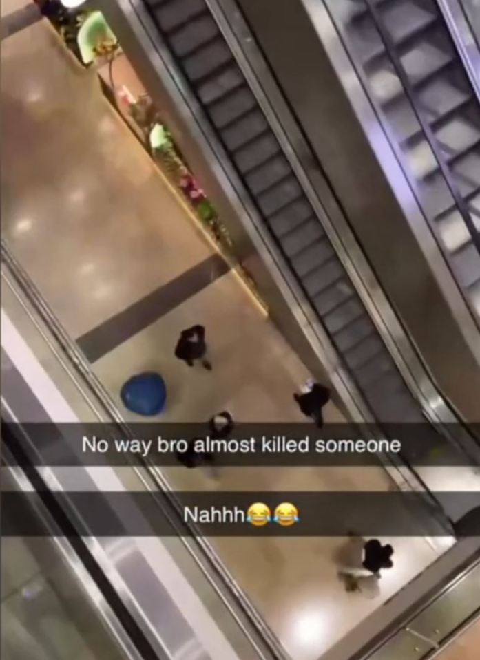 A blue seat lies on the ground of a shopping center, near shoppers, after being thrown from an upper floor.