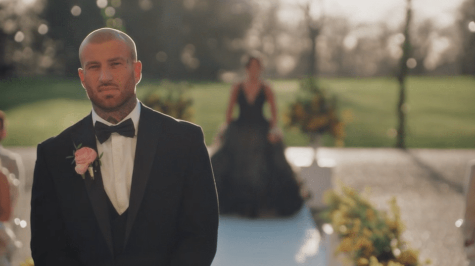 Groom in a tuxedo watching his bride walk down the aisle.