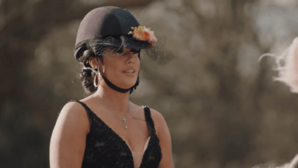 A woman with an equestrian helmet adorned with flowers and a black dress.
