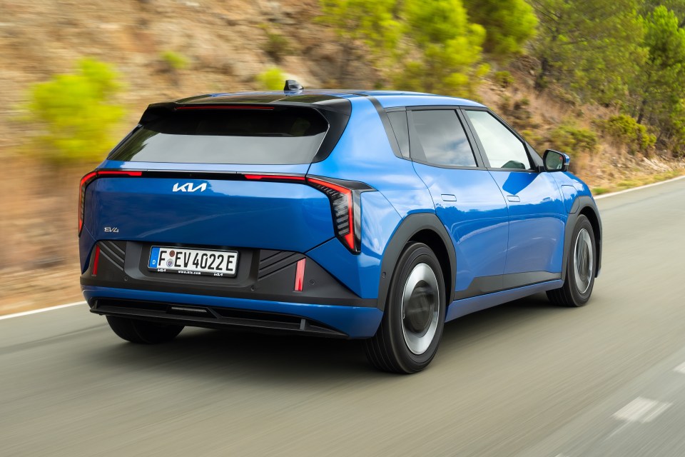 Blue Kia EV3 electric SUV driving on a winding road with trees.