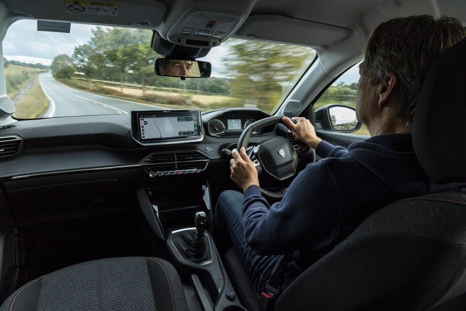 A man drives a Peugeot 208 down a winding country road.