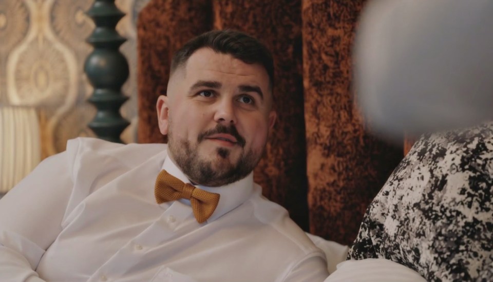 A man with a beard and an orange bow tie, wearing a white shirt, looking towards the right side of the image.