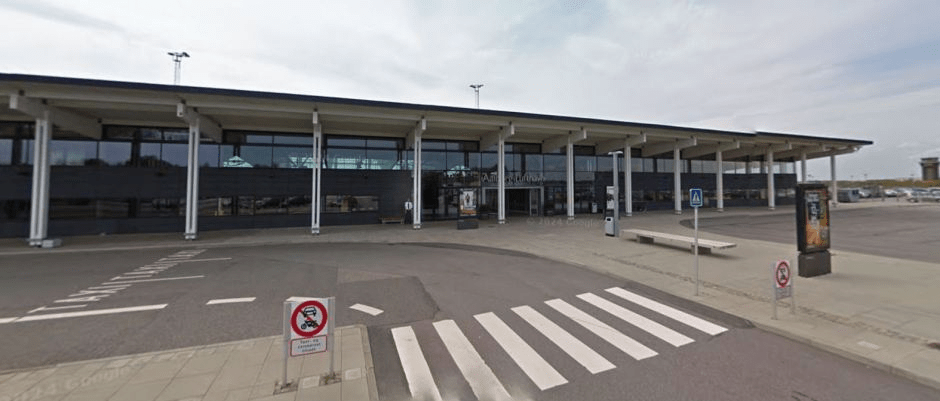 Exterior of a modern airport terminal building with a wide road in front and a crosswalk.