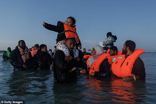 Migrant families as they wade into the water to get a 'taxi boat' to take them to the UK in Gravelines, France
