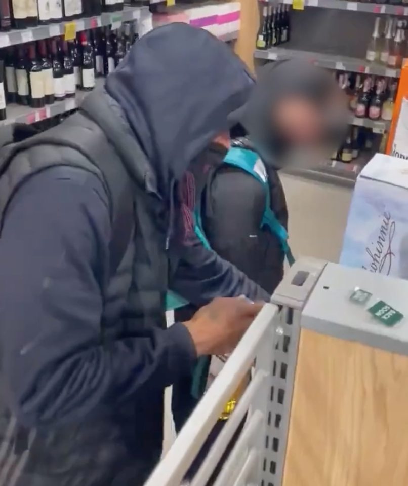 Two people, one blurred, shoplifting bottles of alcohol in a store aisle.