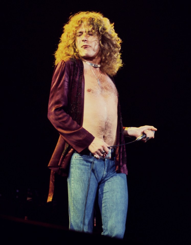Robert Plant performing on stage with an open jacket and jeans.