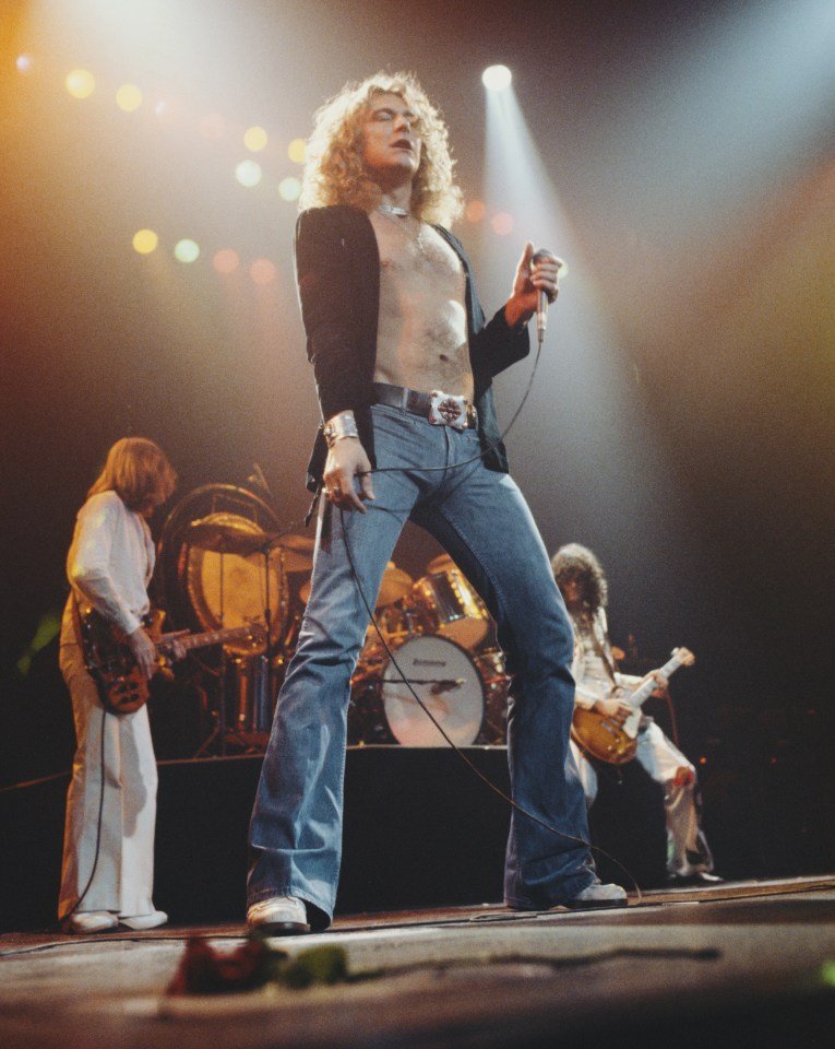 Robert Plant performing on stage with Led Zeppelin, with other band members in the background.