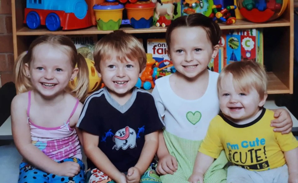 Photo of four young children sitting in front of a shelf of toys.